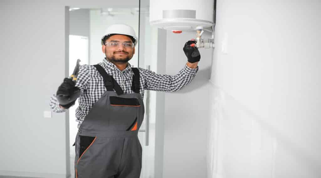 plumber using screwdriver while fixing boiler or water heater, working on heating system in apartment