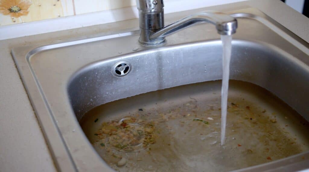 Stainless steel sink plug hole close up full of water and particles of food