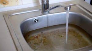 Stainless steel sink plug hole close up full of water and particles of food